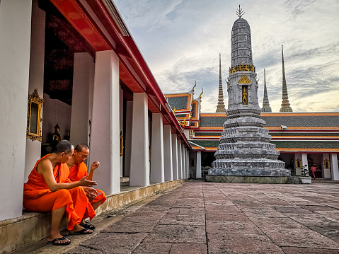 Bangkok, Thailand - September 9, 2019: Two buddhist monks seated at Wat Pho Buddhist temple in Bangkok. Wat Pho is one of the largest and oldest temples in Bangkok and is home to the famous Reclining Buddah. The temple is also known as the birthplace of traditional Thai massage.