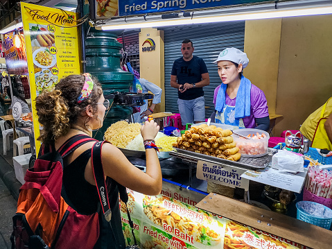 Bangkok, Thailand - September 9, 2019: Vendor cooking food on the street at Khao San road with a tourist woman client