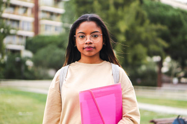 istock Serious hispanic teen standing outdoors at university capus looking at camera with his googles. Portrait of pretty school girl. 1421852964