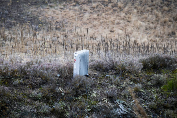 An electrical heater dumped in grassland with dry bushes and wired fence. Concept of illegal rubbish dumping in environment. An electrical heater dumped in grassland with dry bushes and wired fence. Concept of illegal rubbish dumping in environment. space heater stock pictures, royalty-free photos & images