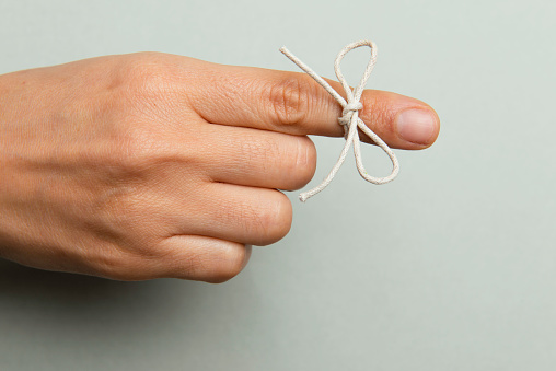 Hand and string tied on index finger on gray background.