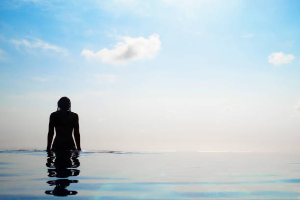 Woman relaxing in infinity swimming pool looking at view stock photo