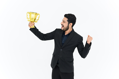 Portrait of Winning businessman celebrating with trophy award for success in business isolated on white background. Successful employee holds golden cup. Looking at the camera.