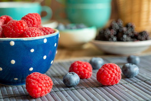 Rapsberries in blue bowl on a table with decoration with Blueberries and Blackberries