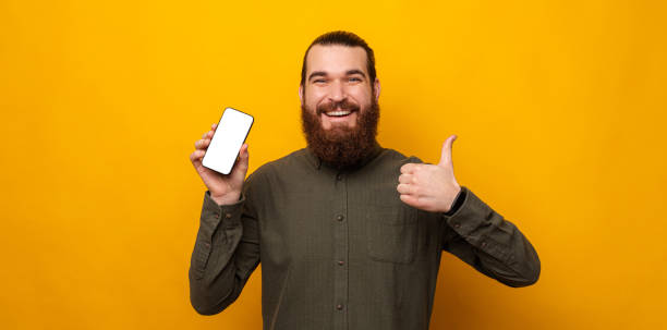 istock Ecstatic bearded man shows phone screen to the camera and thumb up beside. 1421873818