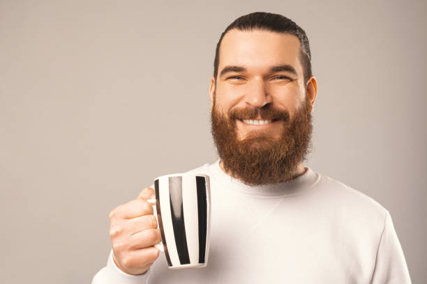 Close up portrait of a bearded man holding a mug and smiling at the camera. stock photo