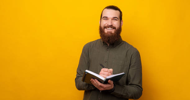 istock Content bearded man smiles at the camera while holding a planner and a pen. 1421873941