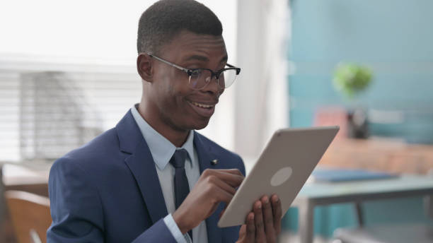 istock Young African Businessman Celebrating Success on Tablet 1421875533