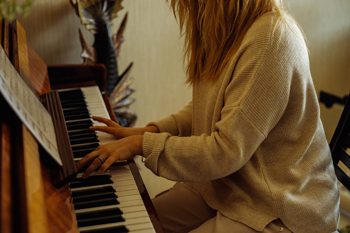 Beautiful blonde woman in home clothes sitting at piano, pressing chord and playing melody top view. Young lady practice playing musical instrument at home. Music education and useful activity.