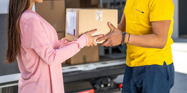 Delivery service, courier giving customer cardboard box, close up on hands. Postal worker and customer standing near truck, online order shipment