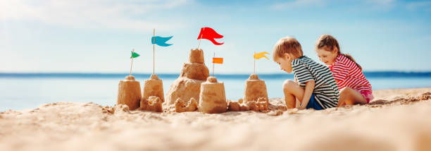Boy and girl playing on the beach on summer holidays. Boy and girl playing on the beach on summer holidays. Children building a sandcastle at the sea. sand castle stock pictures, royalty-free photos & images