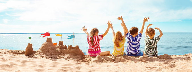 Four happy children sitting on the sea coast and raising up their hands. Concept of the friendship and vacation.