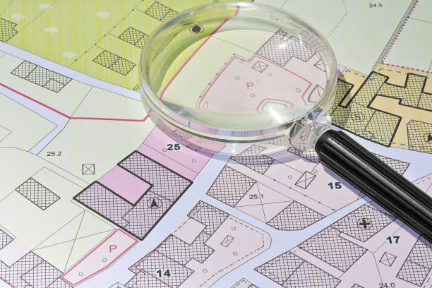 Imaginary cadastral map with buildings, land parcel and vacant plot - property registry and real estate concept seen through a magnifying glass stock photo