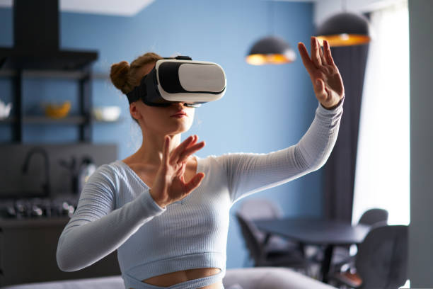 woman in virtual reality goggles enters metaverse, controls immersive experience with hand gestures via headset interface in minimalistic interior. girl gaming in cyber space. futuristic concept. - vrai betis 個照片及圖片檔