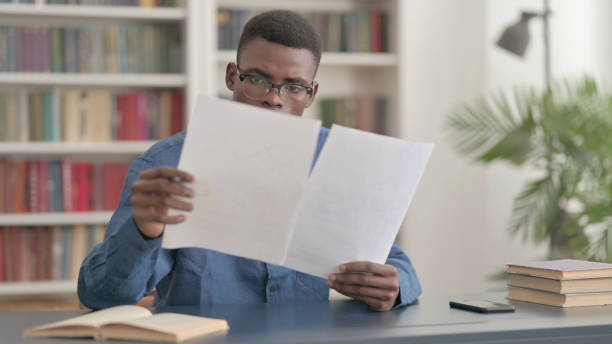 istock Young African Man Reading Reports while Sitting in Office 1421886693