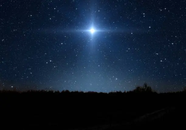 Photo of Bright star, starry sky and forest silhouette. Star indicates the Nativity of Jesus Christ in the starry sky.
