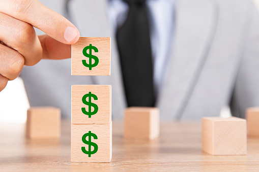 Businessman hand adding wooden cubes with dollar sign