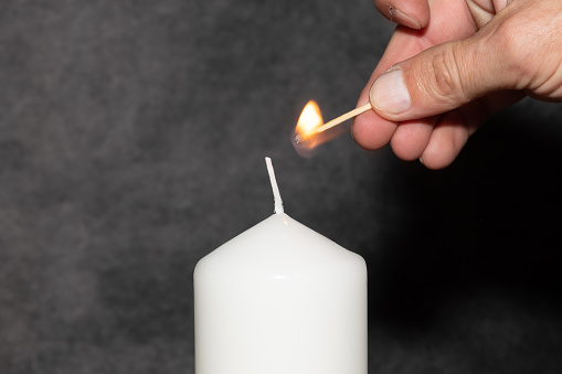 One big white coloured candle with wick burning with yellow flame over dark black background. Apt for use as Diwali and Christmas related wallpapers, greeting cards templates, posters, backdrops. There is no people, no text and copy space.