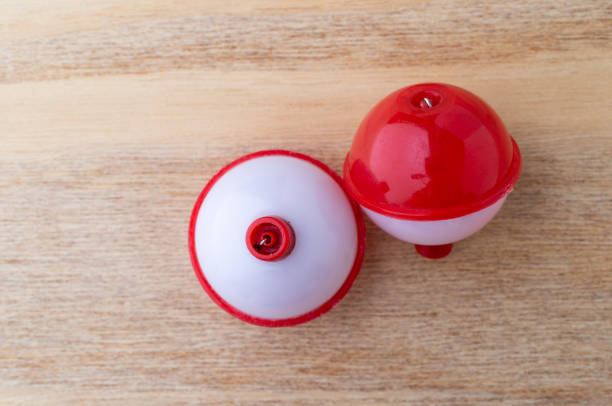 Top view of two red and white plastic fishing bobbers on a wood background.