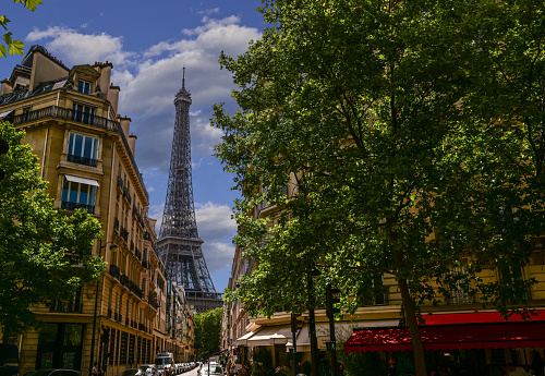 Paris, France. June 2022. Amazing shot of the Eiffel Tower rising between the buildings of the old town and the canopy of trees.