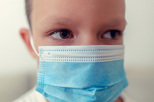 Cropped shot of an 6 years old cute child wearing surgical mask. Child boy wearing protective medical mask during quarantine. Coronavirus covid-19 pandemic.