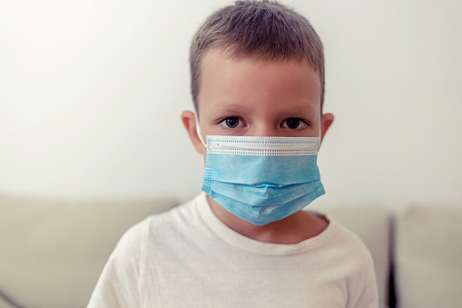 6-7 years old cute child wearing surgical mask. Little boy trying to stay healthy by wearing a mask to protect him against corona virus covid-19.