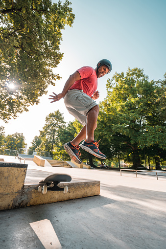 Cheerful Latin man with active lifestyle enjoying an outdoors day in a skate park. He is flying in the air while jumping from a ramp. He is wearing casual clothes.
