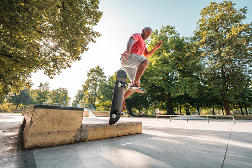 Cool mature latin man exercising with a skateboard outdoors in the city. He is suspended in the air, wearing casual clothes and enjoying a fun time.