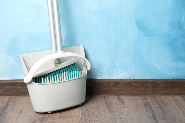 istock Plastic broom with dustpan near light blue wall indoors. Space for text 1421903493