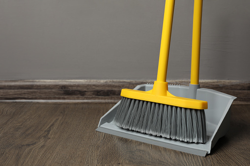 Plastic broom with dustpan near grey wall indoors. space for text
