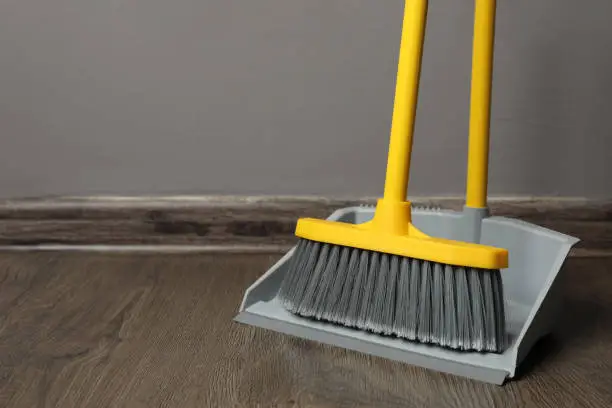 Photo of Plastic broom with dustpan near grey wall indoors. space for text