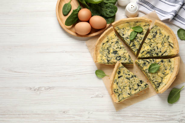 istock Cut delicious spinach pie with ingredients on white wooden table, flat lay. Space for text 1421904004