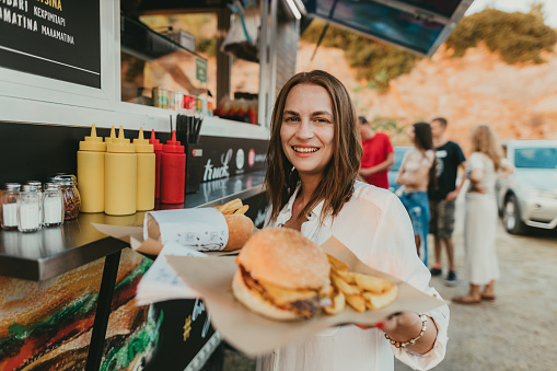 Happy young woman buying burgers and fries at the food truck during her summer vacation