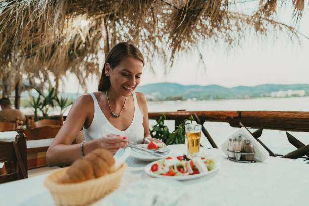 frau sitzt in einem restaurant am meer und isst griechischen salat - mediterranean cuisine mediterranean culture food bread stock-fotos und bilder