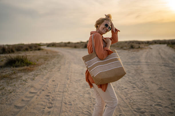 Mature woman carrying a bag is walking on the beach towards the sea on a beautiful sunset.