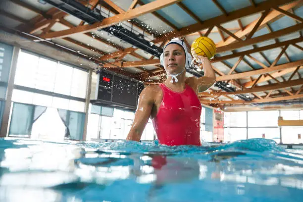 A professional waterpolo player rises from the water to throw the ball.