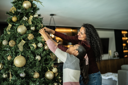 Mother and daughter decorating the christmas tree in the living room at home