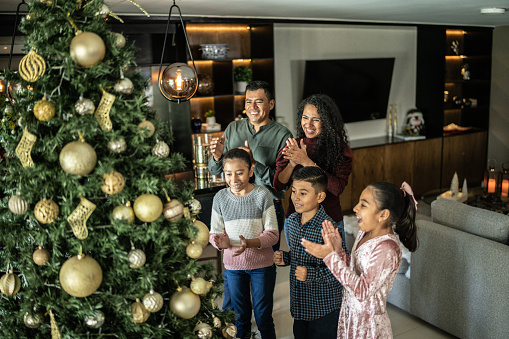 Family clapping while looking to christmas tree in the living room at home