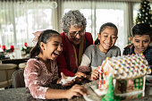 istock Grandchildren decorating a gingerbread house with grandmother for Christmas 1421913258