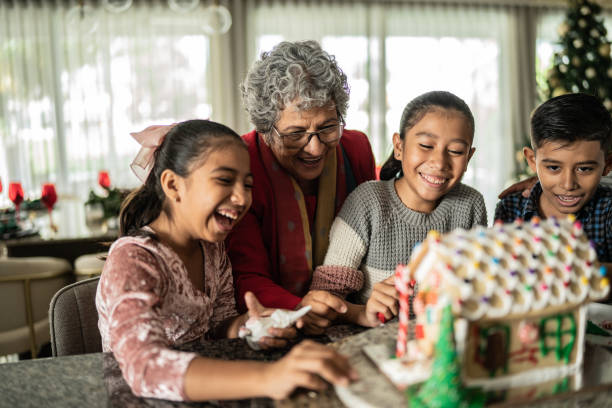 Grandchildren decorating a gingerbread house with grandmother for Christmas stock photo