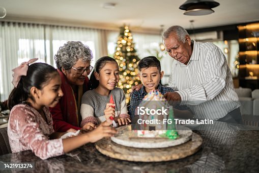 istock Grandchildren making a gingerbread house with grandparents at home 1421913274