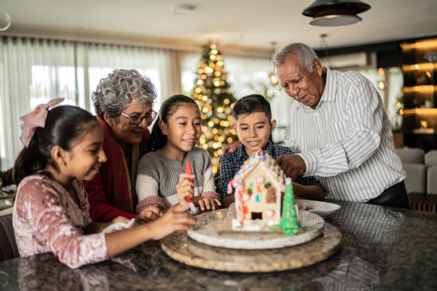 Grandchildren making a gingerbread house with grandparents at home stock photo