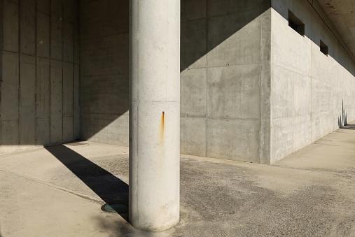 Concrete column on cement sidewalk with solid reinforced concrete wall on behind. Background for copy space.