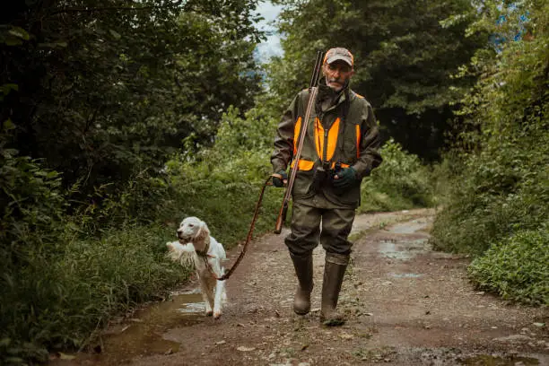 Photo of mature male hunter in modern clothes walking with his dog on dirt road