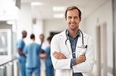 Portrait of a doctor, medicine expert or medical employee smile while standing happy in a hospital with nurse team in background. Professional help, Healthcare worker or surgeon ready for work.