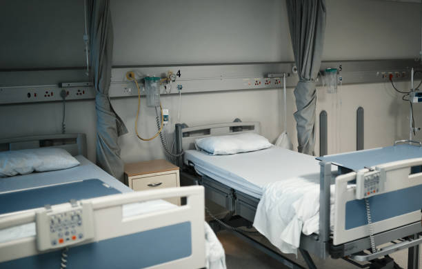 Hospital, bed and healthcare in an empty medical room or ward for health, wellness and medicine. Care, support and trust for rest, recovery and treatment. Still life of a cot or gurney in a clinic Doctor, surgeon and nurse with digital tablet in hospital, clinic and ward for healthcare, medical service and surgery planning online. Portrait of happy indian wellness worker with research analysis night hospital bed stock pictures, royalty-free photos & images