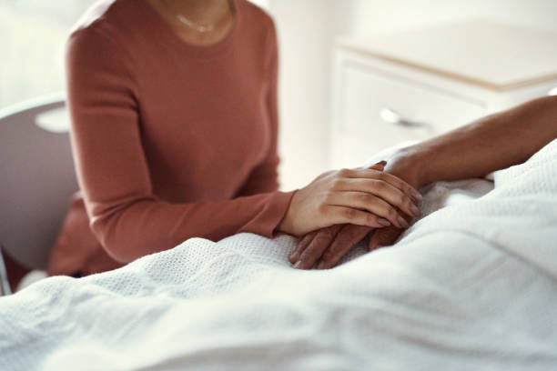 Cancer, healthcare and support with a woman holding hands with her man in the hospital. Medicine, insurance and trust with a couple in a clinic for treatment or help before death, mourning and loss stock photo