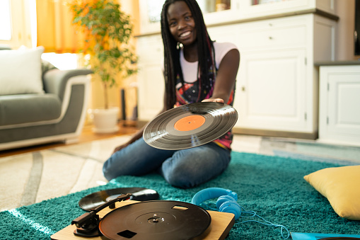 A vinyl record being shown to the camera, by an African-American young woman sitting on the floor by a turntable, focus on the record and retro-style turntable