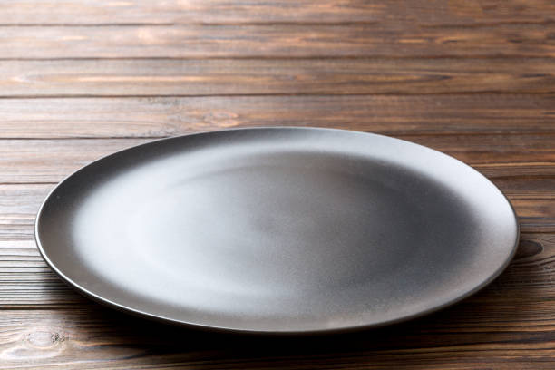 istock Perspective view of empty black plate on wooden background. Empty space for your design 1421925083