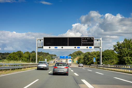 Wiesbaden, Germany - August 26, 2021: Traffic and traffic information system on german Autobahn A66 nearby Wiesbadener Kreuz. Bundesautobahn A66 (abbreviated BAB 66 or A66) is a heavily frequented highway in the Southwest of Germany. It connects the cities of Wiesbaden, Frankfurt and Fulda. Some road users in the background. Some road users in the background.